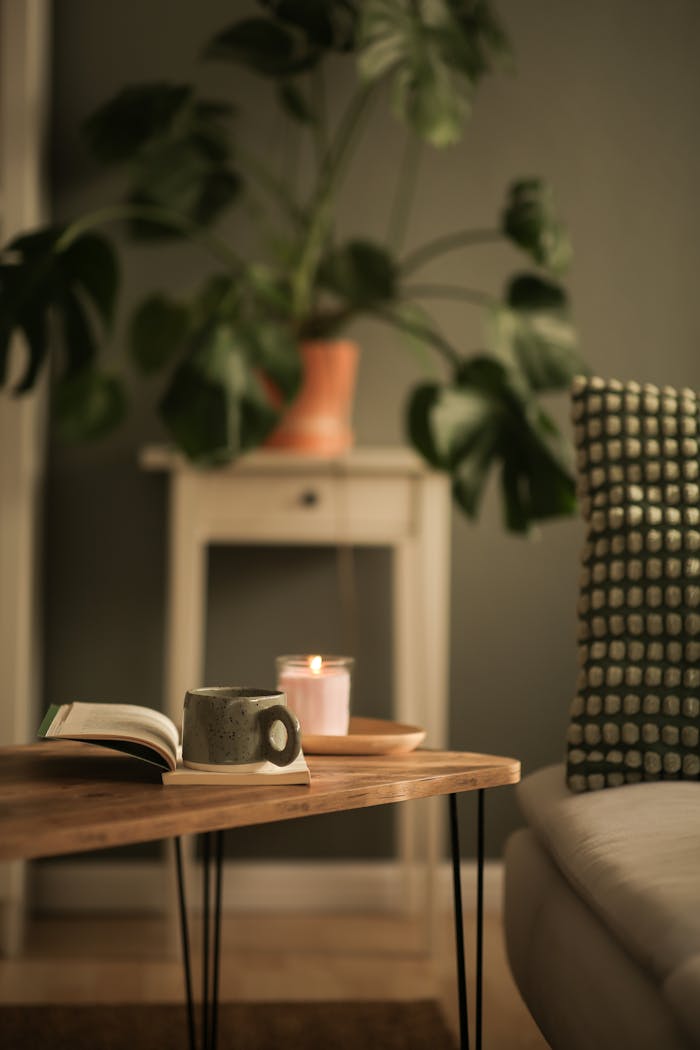 Inviting interior scene featuring a coffee table with a mug, book, and candle beside a lush plant.