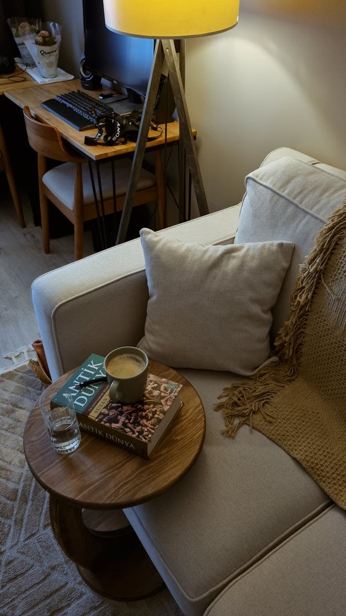 Warm living room corner with sofa, books, coffee, and ambient lighting creating a cozy atmosphere.